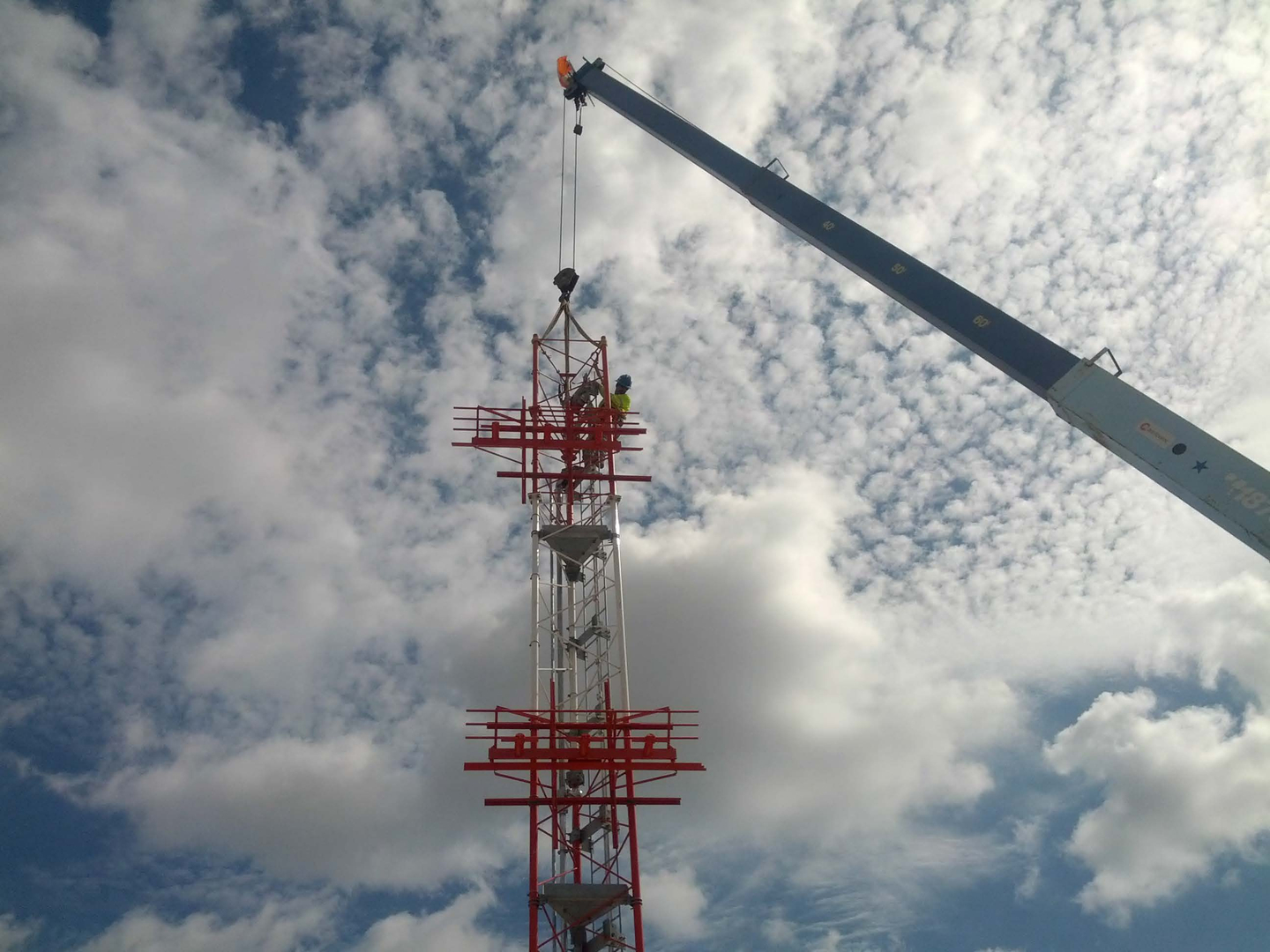 A crane is lifting up the top of a tower.